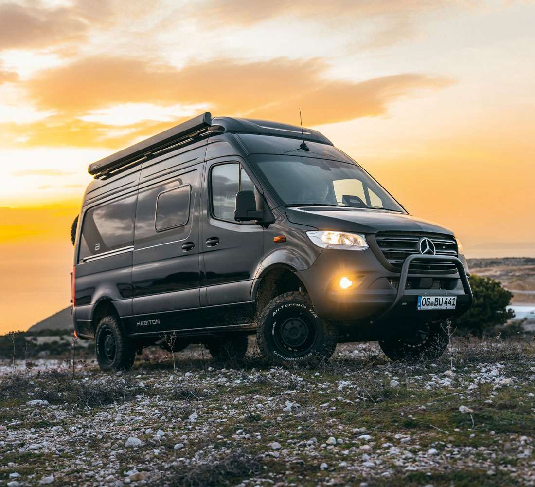 Dunkler Bürstner Habiton Campervan auf Mercedes-Benz Sprinter Basis in felsiger Landschaft bei Sonnenuntergang.