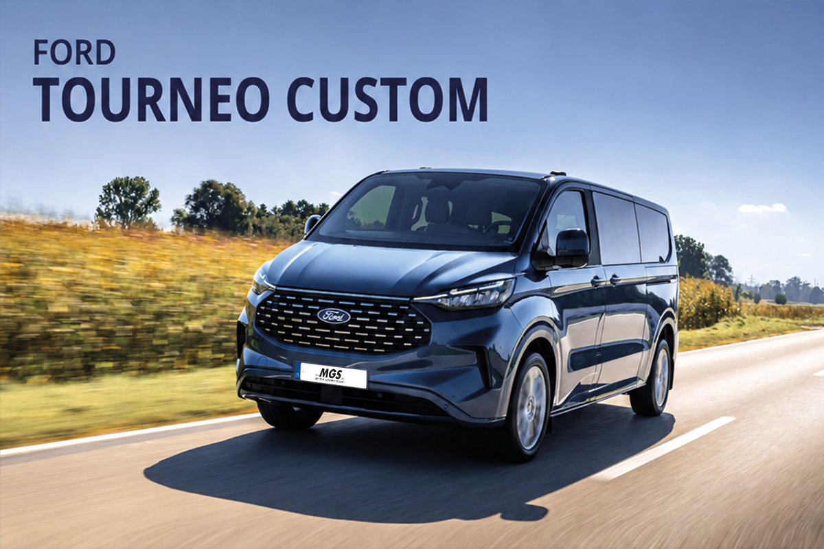 Dunkelblauer Ford Tourneo Custom während der Fahrt auf einer Landstraße, schräg von vorne dargestellt.