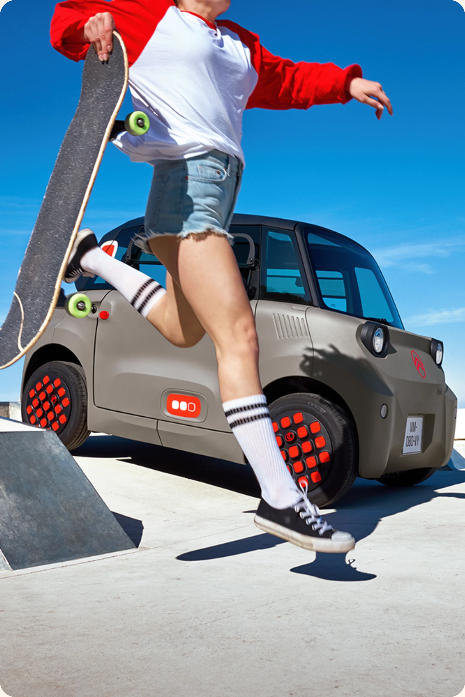 Citroen Ami im Hintergrund, im Vordergrund eine Frau die Tricks mit dem Skateboard macht