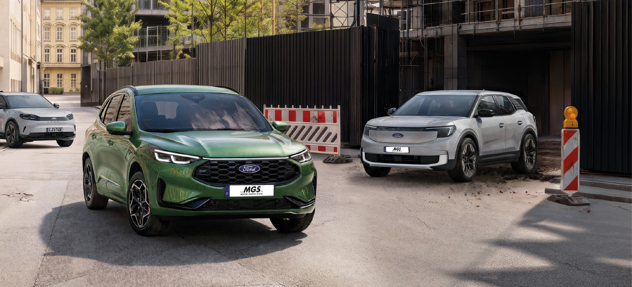 Grüner Ford Kuga und grauer Ford Explorer in städtischer Umgebung vor einer Baustelle.
