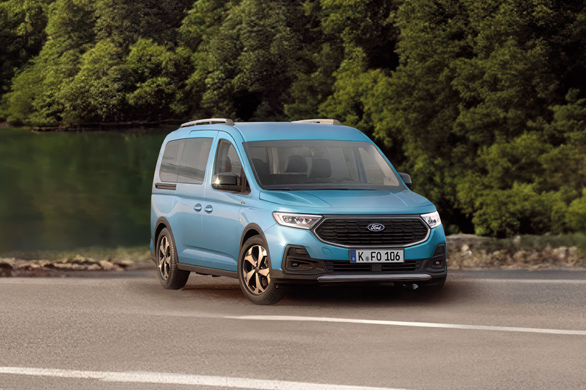 Blauer Ford Tourneo Connect auf einer Straße vor einem See und grüner Waldkulisse.