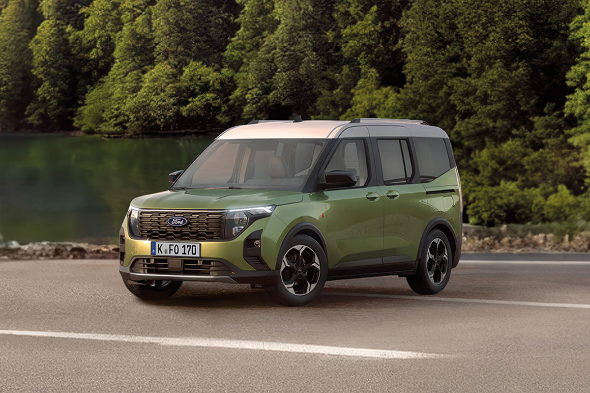 Grüner Ford Tourneo Courier auf einer Straße mit See und Bäumen im Hintergrund.