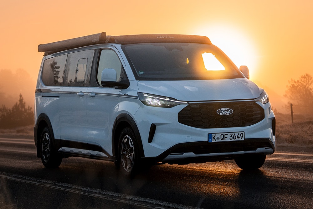 Ford Campervan mit Markise in schräger Frontansicht bei Sonnenuntergang.