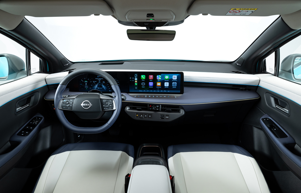 Innenraum des Nissan Leaf mit digitalem Cockpit, großem zentralen Touchscreen, Multifunktionslenkrad und hellen Vordersitzen.