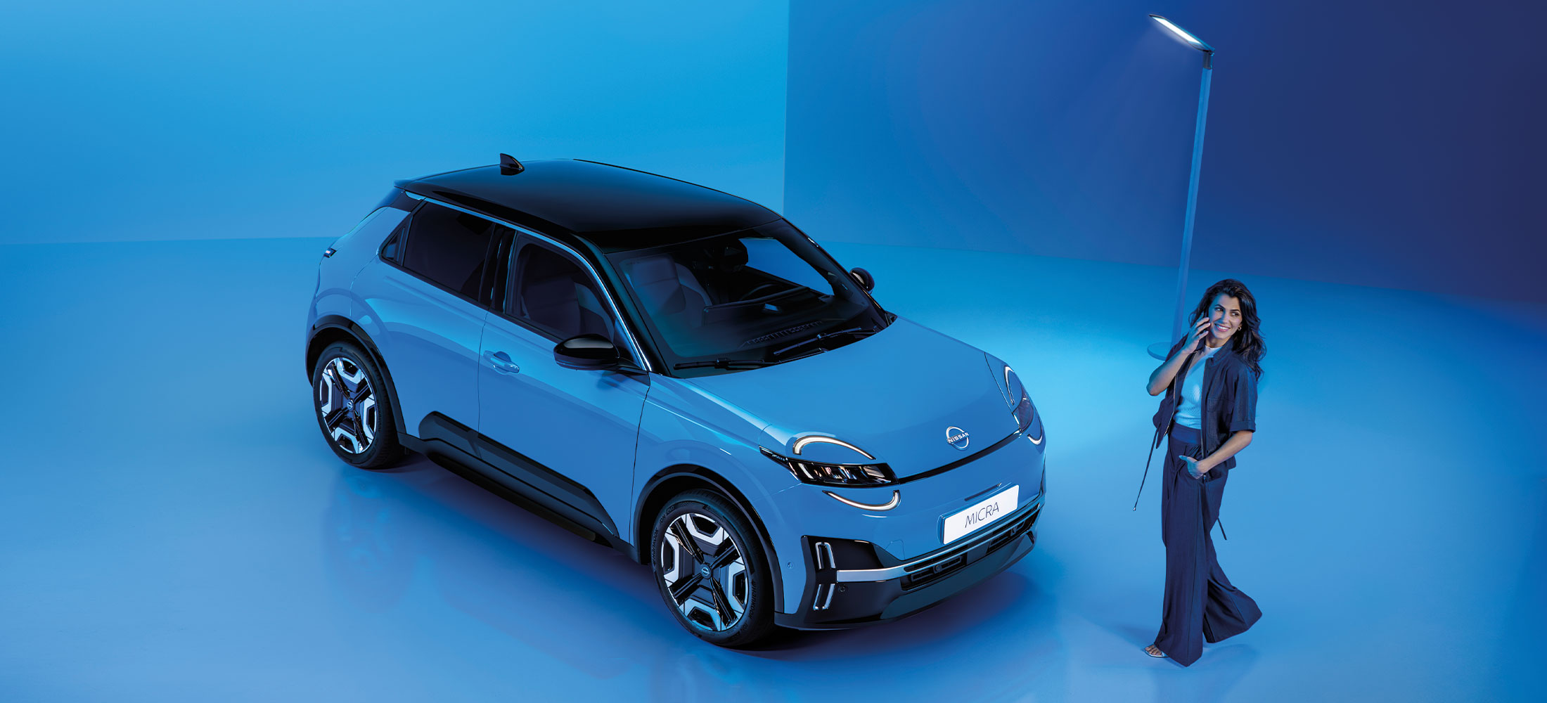 Nissan Micra EV in Blau abgebildet mit einer Frau auf blauem Hintergrund