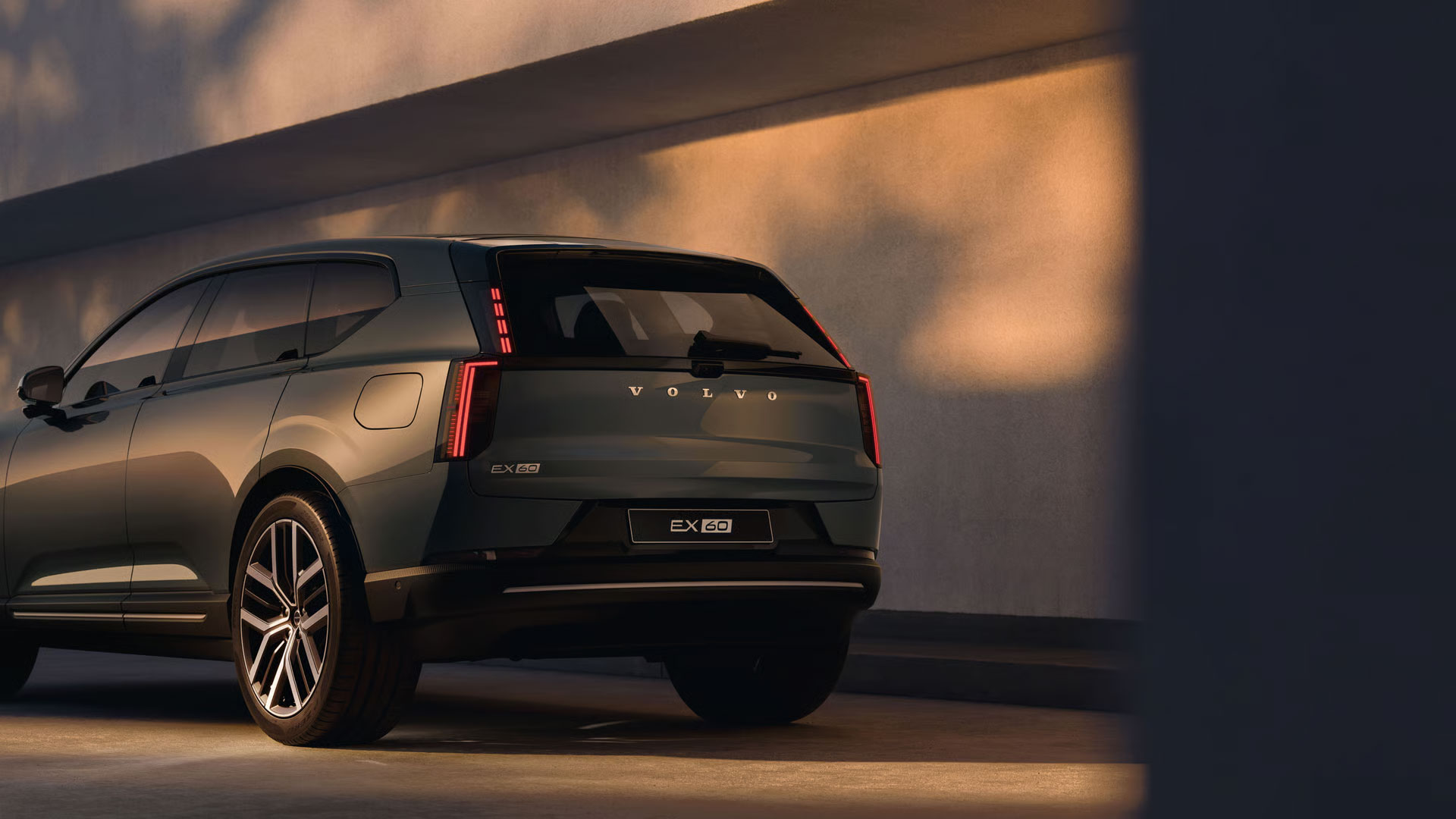 Schräge Heckansicht des Volvo EX60, der vor einer Wand gepark ist.