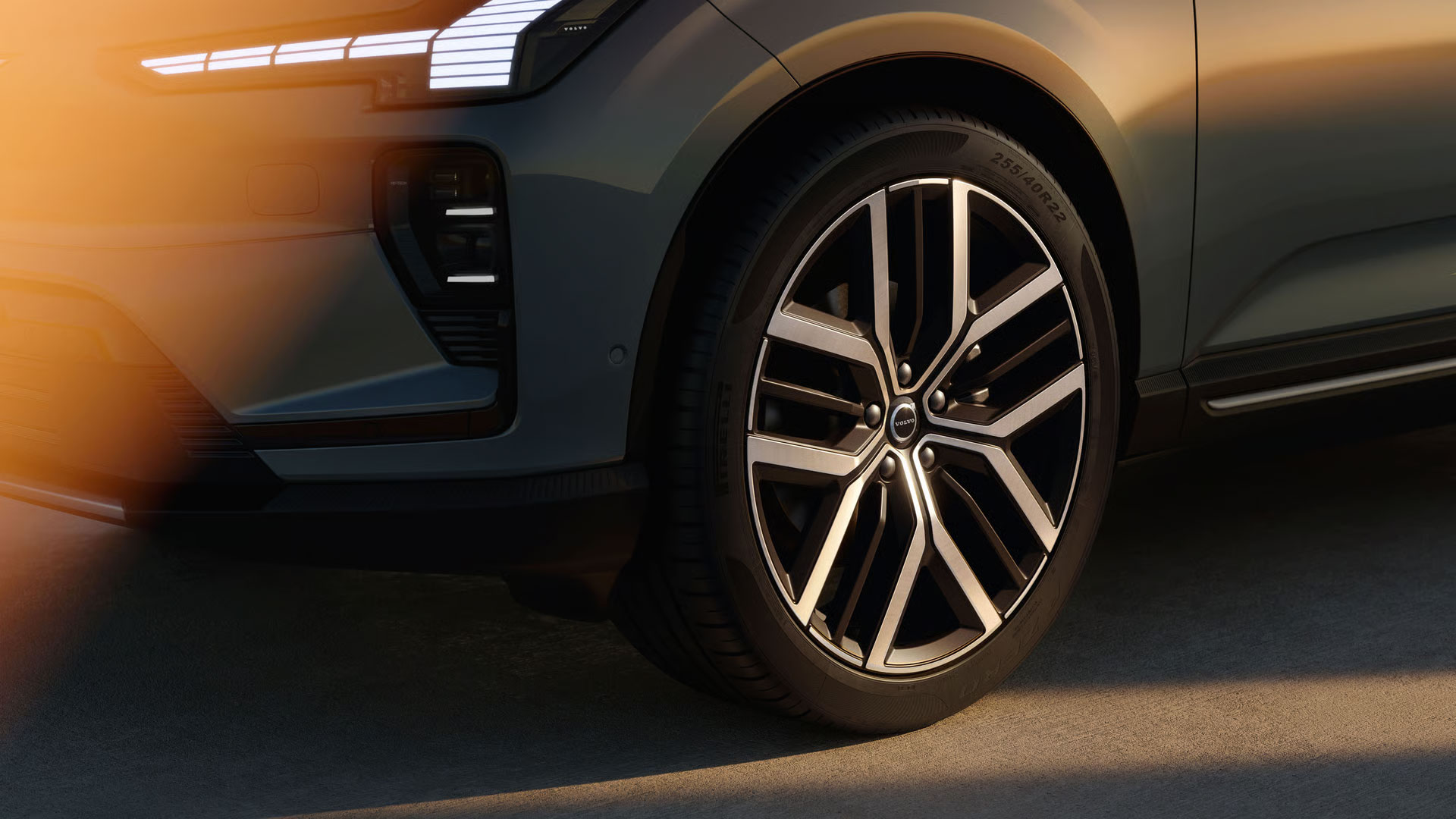 Eine Nahaufnahme des Vorderrads des Volvo EX60 mit der Scheinwerfersignatur, die im warmen Abendlicht sichtbar ist.
