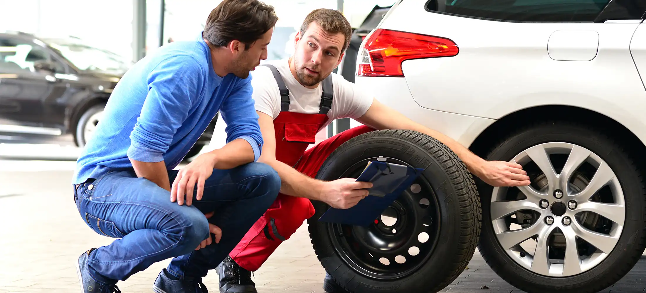 ein Mitarbeiter der einem Kunden zeigt wie man Reifenwechselt